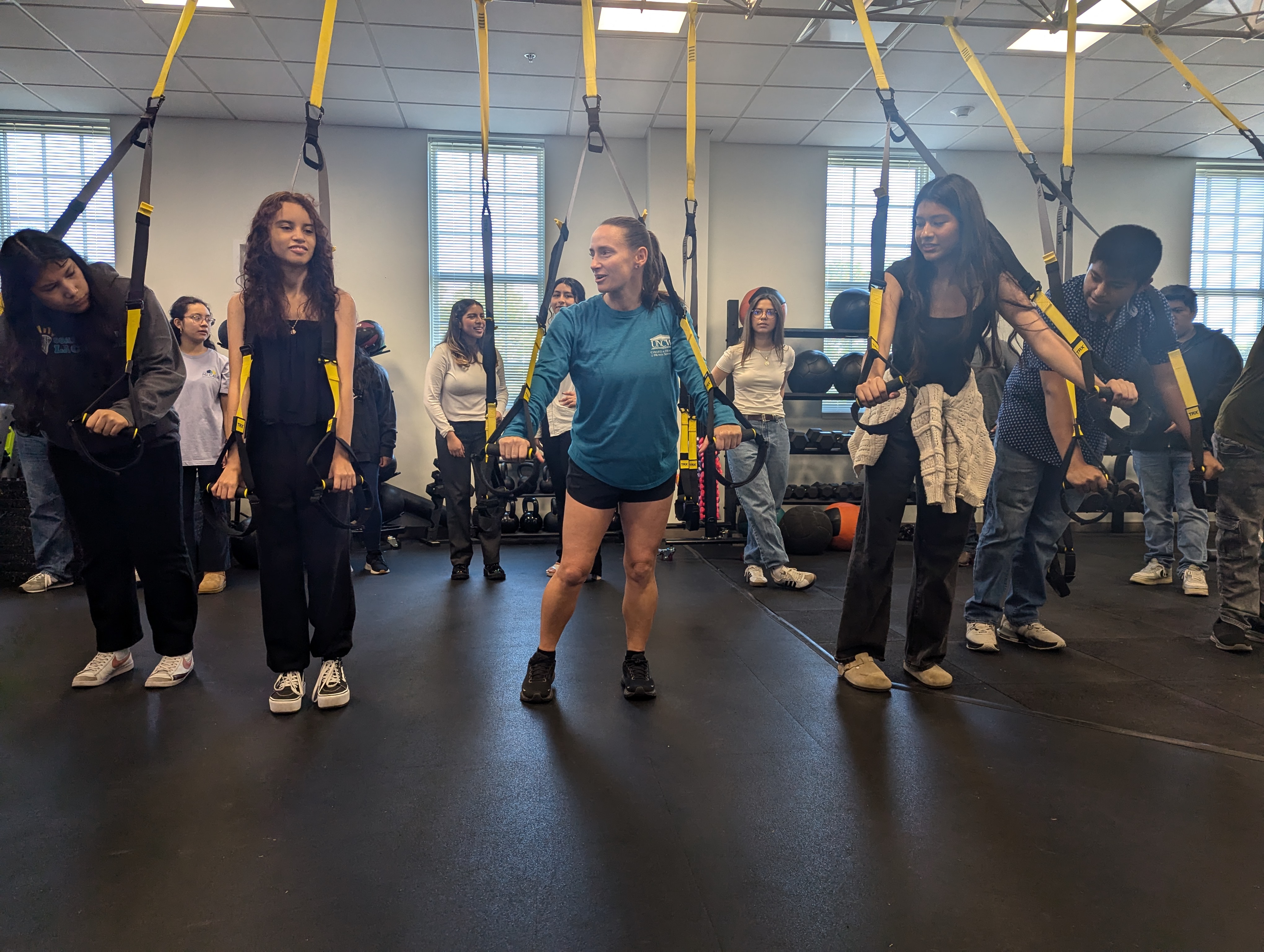 A university faculty member guides local high school students through a TRX workout.